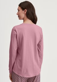 Lange mouw, ronde hals T-shirt van lichtroze katoen, met een afgeronde zoom. G gedragen met geprinte pyjamabroek.