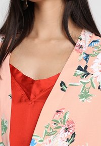 Blommig kimono i rosa tyg med stora färgglada blommor. Röd satin topp med V-ringning som syns under.