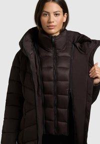 Schwarze Daunenjacke mit hohem Kragen und Reißverschluss vorne. Verfügt über gesteppte Abschnitte und ein geschichtetes, oversized Design für zusätzliche Wärme.