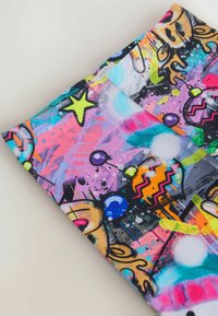 Väritetty kangas, jossa on graffitityylisiä abstrakteja kuvioita, mukaan lukien tähtiä, muotoja ja sarjakuvamaisia kissan kasvoja vaalealla taustalla.