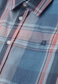 Camicia a quadri blu, grigia e rossa con bottoni bianchi e piccolo logo geometrico ricamato blu navy sul petto.