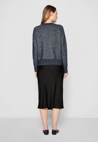 Pullover blu navy in maglia con finitura testurizzata, orlo a coste e spalle cadenti, abbinato a una gonna nera in satin lunga fino al ginocchio. Ballerine nere.