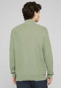 Pull vert clair en tricot avec un motif texturé, manches longues et col montant. Poignets et ourlet côtelés en tissu uni.
