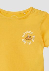 Geel baby t-shirt met een kleine oranje auto en giraffe graphic, en witte tekst met "De hele dag plezier" vlakbij de hals.