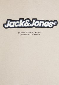 Camiseta de algodón beige con el audaz logo en negro y blanco de "Jack & Jones" encima del texto, con una textura suave y lisa.