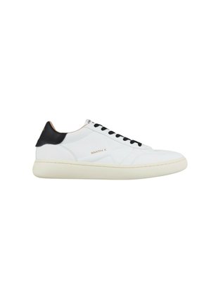 Witte lage sneaker met zwart hieltabblad, zwarte veters, beige zool en "SMITH X" branding aan de zijkant.