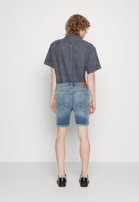 Camisa de manga corta gris con un acabado texturizado, combinada con pantalones cortos de mezclilla azul claro con dobladillos enrollados y un parche de cuero marrón en la cintura.