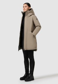 Beige geïsoleerde parka met een hoge kraag, een rits aan de voorkant en zijzakken, gecombineerd met zwarte leggings en kniehoogte laarzen. Zachte textuur.