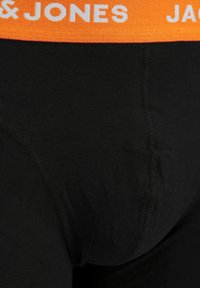Black cotton boxer briefs with an orange elastic waistband featuring white text. Smooth texture with visible stitching detail.