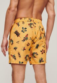 Pantaloni da mare gialli con stampa tropicale che presenta pesci, fiori e pagode. Vita elasticizzata con tasca posteriore per riporre oggetti.