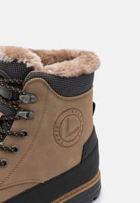 Braune Wildleder-Ankle Boots mit einem schwarzen strukturierten Kragen, Futter aus Fell und schwarzer Gummisohle. Verfügt über Metallösen und ein Logodetail.