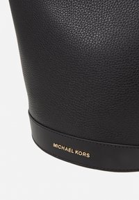 Borsa in pelle nera con finitura testurizzata, caratterizzata da una base in pelle liscia e un logo "MICHAEL KORS" in rilievo dorato.