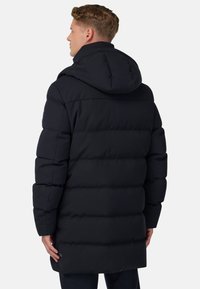 Svart puffjacka med huva, med quiltade sektioner, rak skärning och en logotypdetalj på nedre vänstra sidan. Mjuk, isolerad textur.