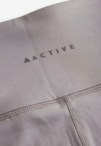 Tessuto attivo grigio con una texture liscia, un logo stampato "ACTIVE" e dettagli di cucitura visibili.