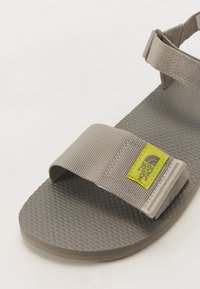Grey sandal with textured rubber sole, fabric straps, and a yellow logo tag from The North Face. Features adjustable ankle strap.