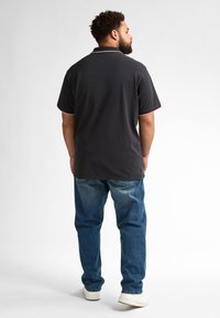 Czarna koszulka polo z kontrastującymi czerwonymi wykończeniami, w połączeniu z niebieskimi dżinsami. Model zwrócony plecami, prezentujący kołnierzyk koszulki oraz luźny krój.