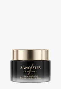 Tarro de vidrio negro con tapa de metal dorado. La etiqueta presenta texto en blanco y dorado; el producto se llama "Lancaster Golden Lift." Crema para uso nocturno.