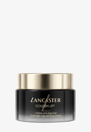 Barattolo di vetro nero con un coperchio in metallo dorato. L'etichetta presenta un testo bianco e dorato; prodotto chiamato "Lancaster Golden Lift." Crema da utilizzare durante la notte.