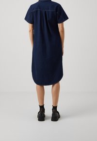 Marinblå denimskjortklänning med korta ärmar, rundad nederkant och synliga sömmar, matchad med svarta platåskor och strukturerade strumpor.