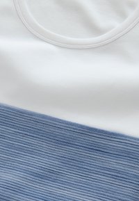 Maglietta di cotone con scollo rotondo; metà superiore in bianco solido, metà inferiore in azzurro chiaro testurizzato con strisce orizzontali.