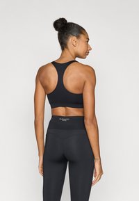 Μαύρο αθλητικό σουτιέν με σχεδιασμό racerback, συνδυασμένο με μαύρο κολάν ψηλής μέσης που διαθέτει ραφές και λογότυπο στη μέση.