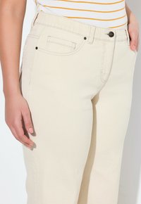 Pantalones de mezcla de algodón color beige claro con un diseño de pierna recta, que cuentan con un bolsillo frontal, costuras en contraste y un cierre de botón.
