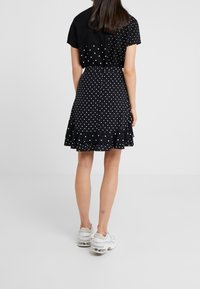 Jupe noire à pois avec un ourlet volanté, assortie à un haut noir uni. Comprend des manches courtes, un design décontracté et une taille cintrée.