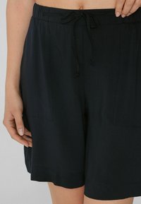Pantalones cortos negros fabricados con tejido ligero, con una cintura elástica con cordón y dos bolsillos laterales en cada lado.