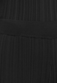 Tissu noir structuré avec des motifs verticaux et une ceinture lisse et élastique. La texture semble ajustée et extensible.