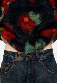 Miękki czarny sweter z czerwonymi, zielonymi i niebieskimi wzorami, zestawiony z ciemnoniebieskimi dżinsami z złotym przeszyciem i metalowym guzikiem.