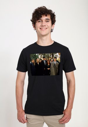 Black T-shirt featuring a rectangular image of a group of people in dark clothing outdoors, surrounded by greenery.