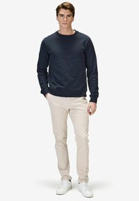 Navy sweatshirt med rundhals och ribbade ärmar, kombinerad med ljusbeiga smala byxor och vita sneakers. Slät textur, avslappnad design.