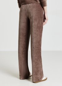 Pantaloni marroni a gamba larga realizzati in morbido tessuto di velluto a coste con costine verticali. Presentano una vita elastica e una texture liscia.