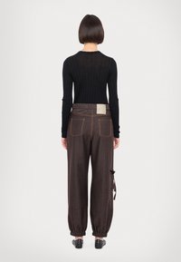 Haut noir à manches longues côtelé et pantalon large à rayures brunes avec des poignets élastiques. Détails notables : un patch en tissu sur la ceinture.