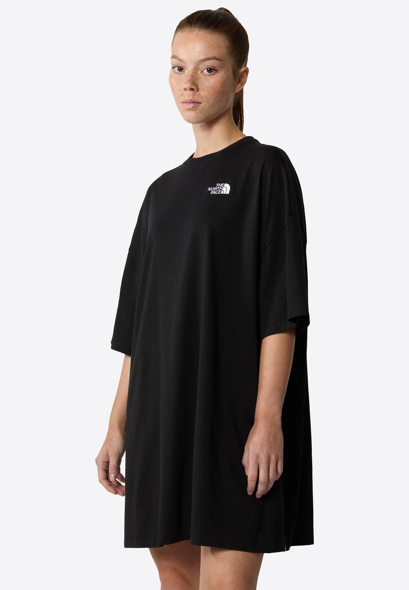 Melna oversize T-krekla kleita, kas izgatavota no kokvilnas, ar īsām piedurknēm un baltu logo kreisajā krūtī, ar brīvu piegulšanu un sānu šķirbnēm.