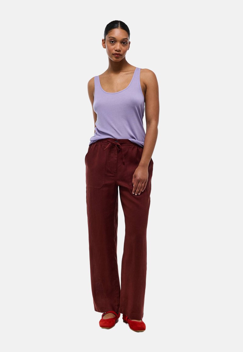 Débardeur violet clair associé à un pantalon bordeaux ample avec cordon de serrage, et ballerines rouges. Tissu doux avec une coupe décontractée.