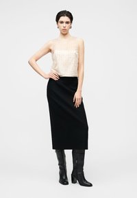 Haut sans manches beige à motifs ponctués, associé à une longue jupe noire et des bottes noires à talons montant jusqu'aux genoux. Silhouette simple et moderne.