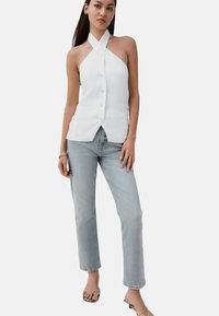 Fehér lenből készült pántos felső keresztbe font nyakrésszel, elől gombos és lekerekített szegéllyel. Világoskék egyenes szárú farmerrel és szandállal párosítva.