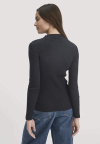 Schwarzes, geripptes Langarmoberteil mit hohem Kragen, taillierter Passform und strukturiertem Stoff, kombiniert mit lockeren blauen Jeans.