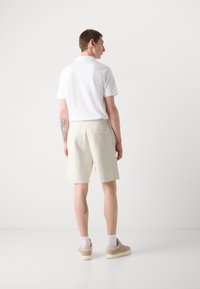 Camisa polo blanca de manga corta, combinada con pantalones cortos beige de rayas. Presenta un bolsillo trasero y zapatillas beige con calcetines.