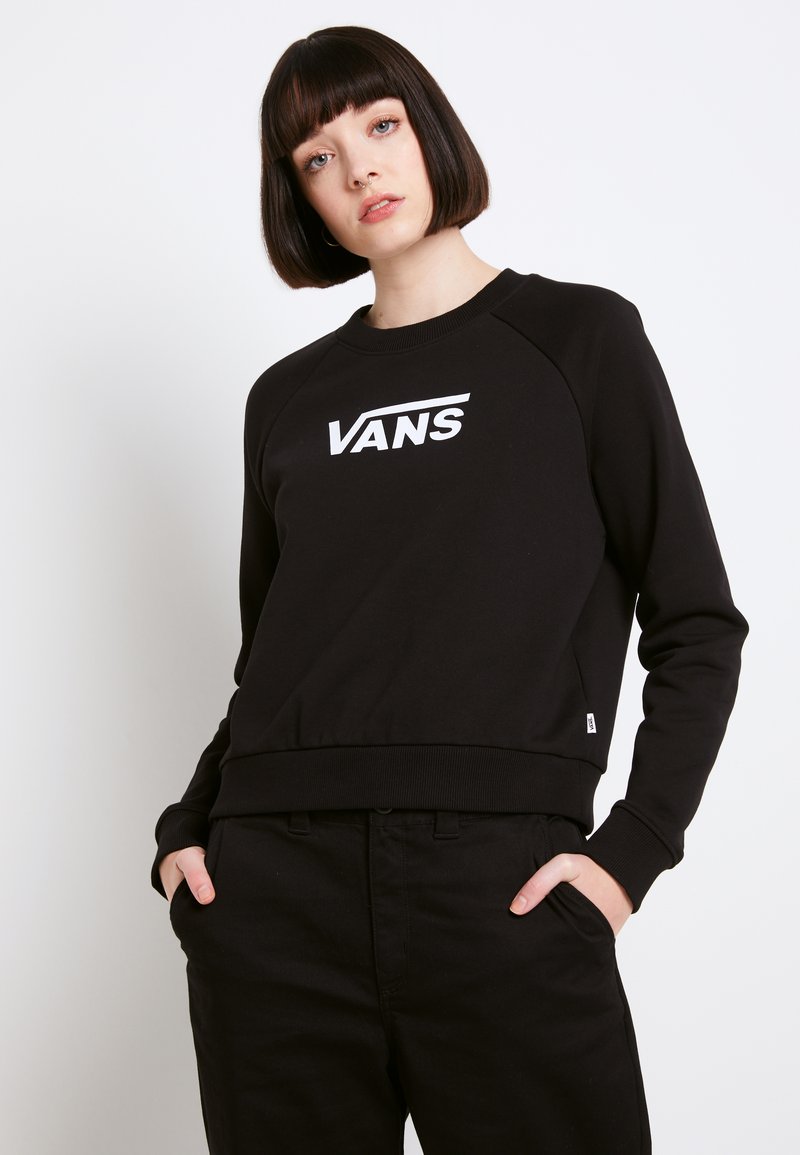 Sudadera negra con un logo blanco de "VANS", con cuello redondo, mangas raglán y puños de canalé, combinada con pantalones negros.