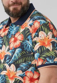 Korte mouwen polo shirt met een levendig, gekleurd bloemenpatroon van hibiscus en tropische bladeren op een donkere achtergrond. Marineblauwe kraag.