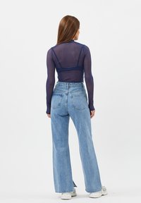 Top trasparente blu navy a maniche lunghe abbinato a jeans a vita alta di un leggero blu chiaro con gamba larga. L'outfit presenta una vestibilità casual e texture morbide.