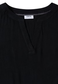 Haut noir à manches longues avec un col rond fendu et une texture verticale subtile, avec une étiquette blanche portant le nom de la marque "CECIL" à l'intérieur du col.