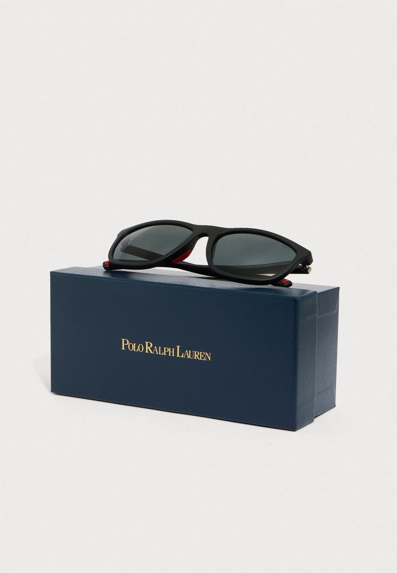 Black sunglasses with grey lenses feature a sleek frame. Presented atop a navy box, embossed with "Polo Ralph Lauren" in gold.