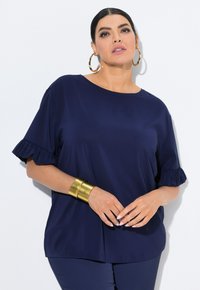 Top blu navy a maniche corte con dettagli arricciati, realizzato in tessuto liscio. Presenta un collo rotondo ed è abbinato a accessori dorati.