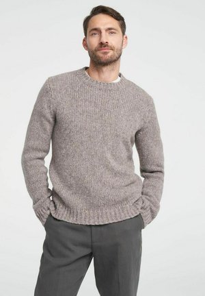 Lichtgrijze gebreide trui met een ronde halslijn, geribde manchetten en zoom, met een gestructureerde, zachte afwerking. Gedragen over een wit shirt.