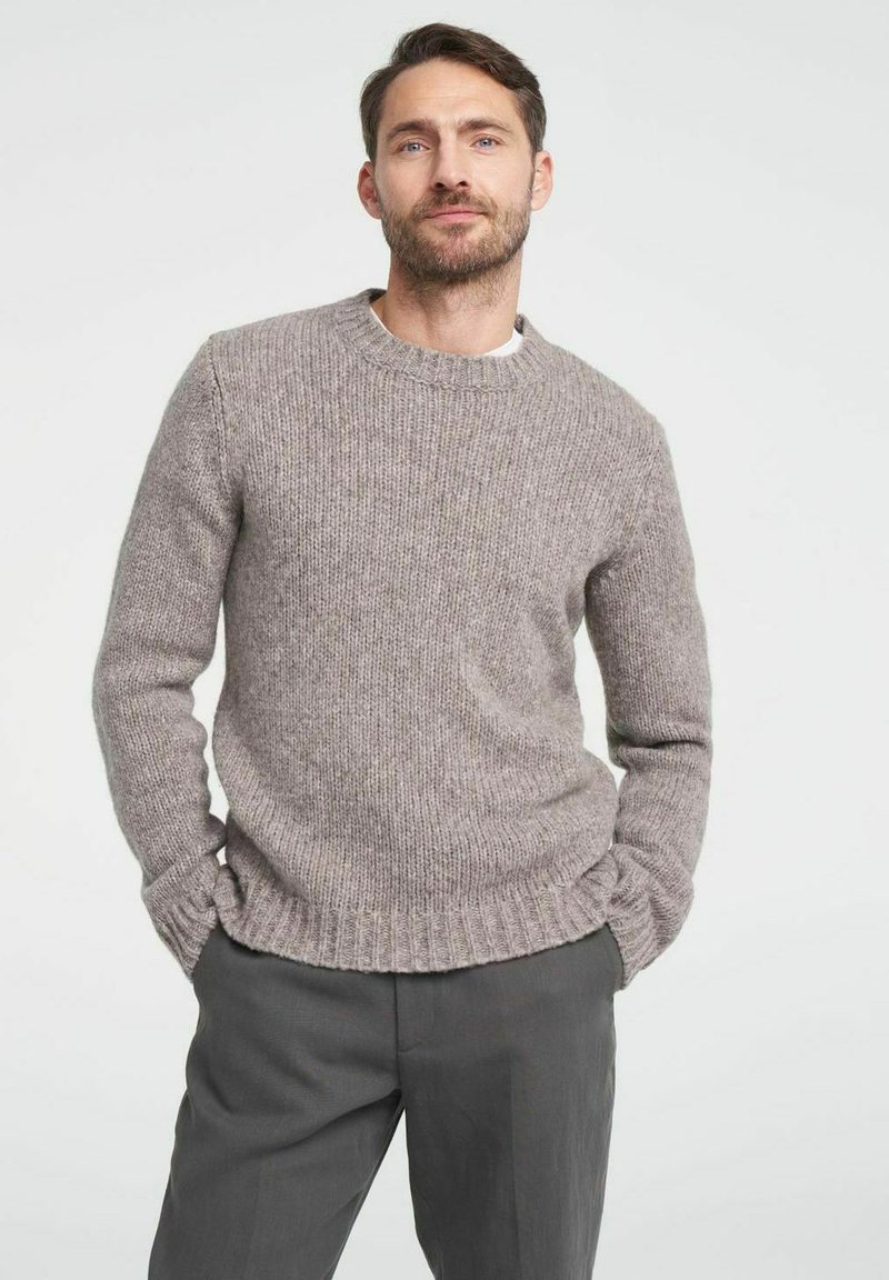 Hellgrauer, gestrickter Pullover mit Rundhalsausschnitt, gerippten Bündchen und Saum, ausgestattet mit einer strukturierten, weichen Oberfläche. Über einem weißen Hemd getragen.