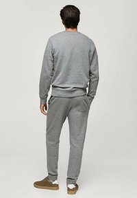 Hanorac gri și pantaloni de trening asortați, confecționați dintr-un material moale, cu mansete cu nervuri și un detaliu de buzunar pe spate. Pantofii din piele de nubuck completează ținuta.