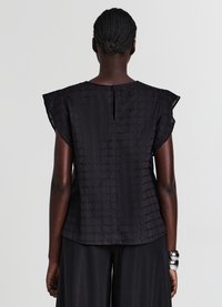 Haut noir à manches courtes avec un motif géométrique texturé, un col rond et une ouverture en forme de goutte dans le dos. Le tissu semble léger et fluide.